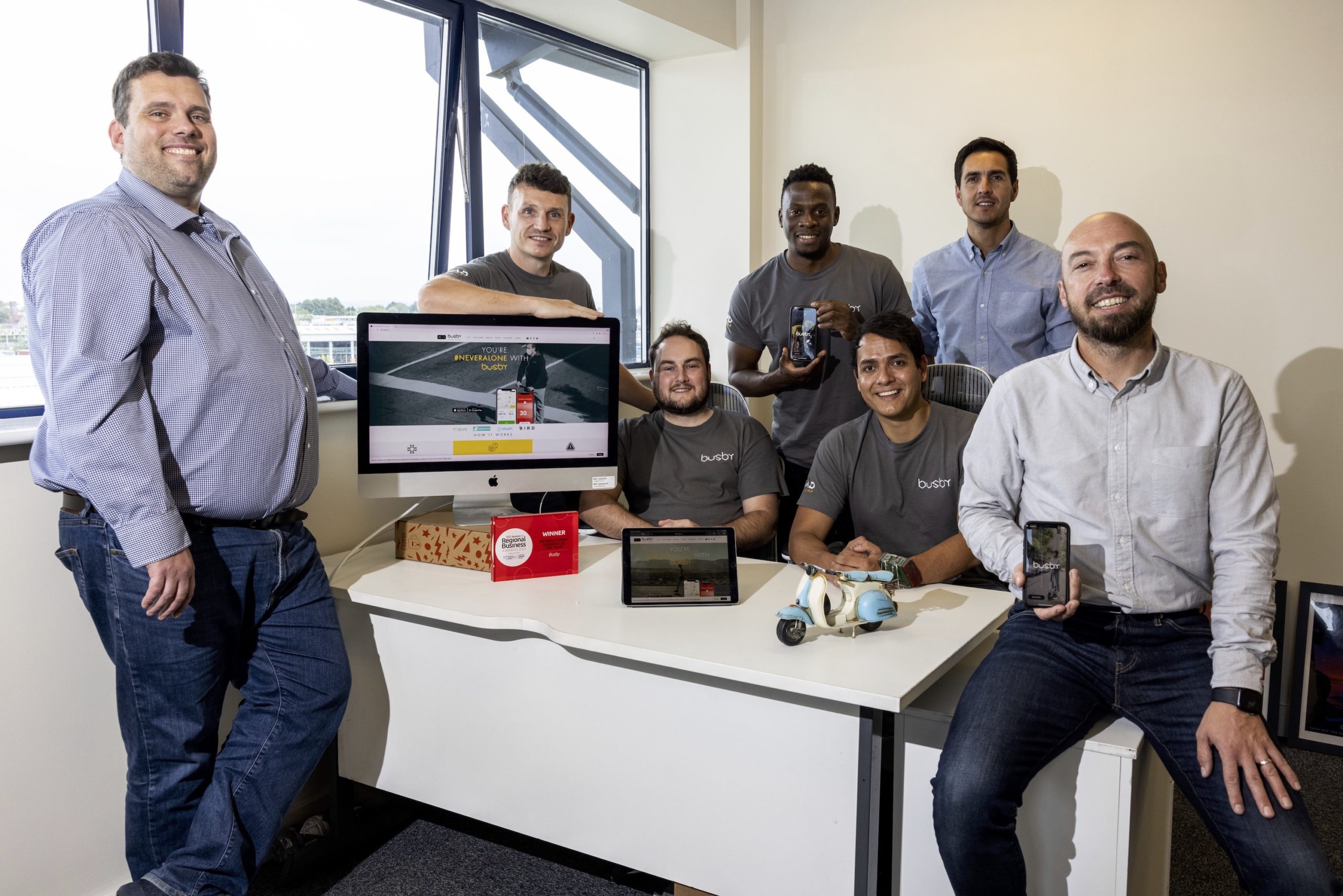Seven men in a room next to a desk showing the computer screen