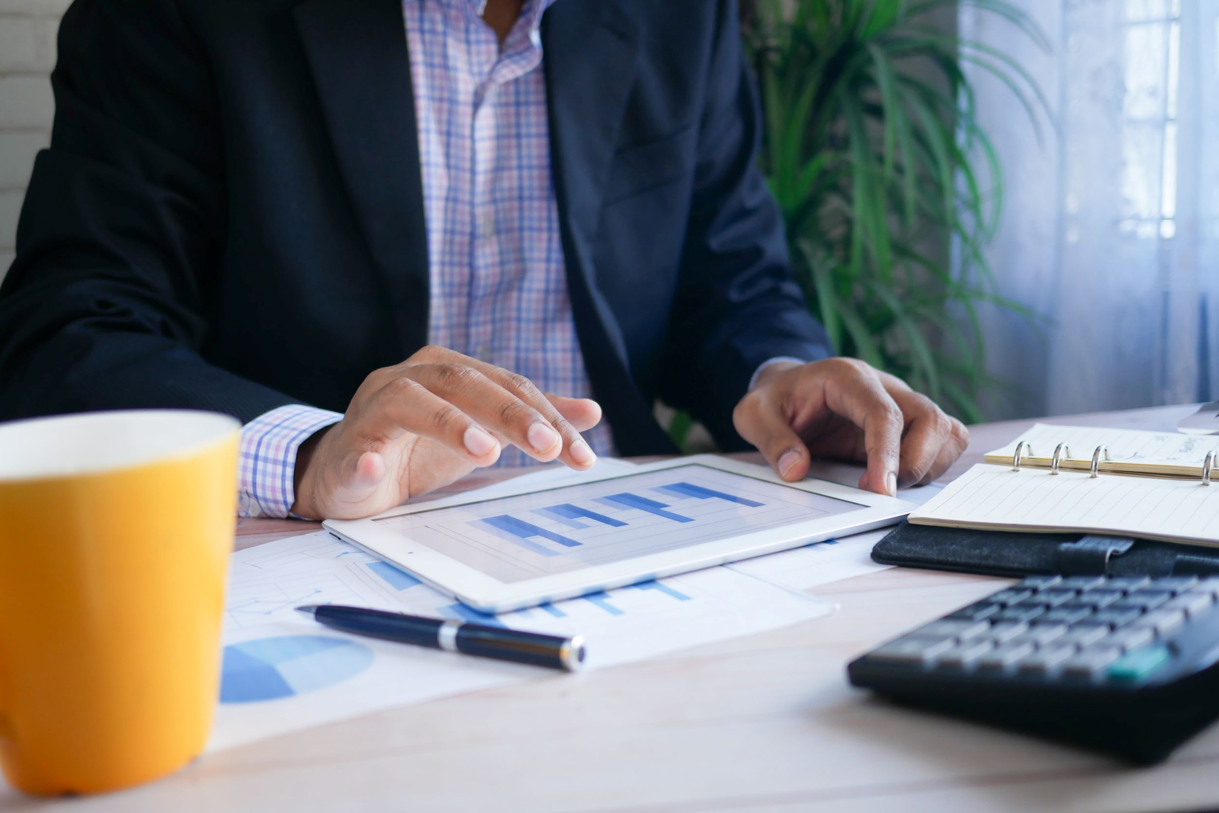 A man in a suit using an iPad with a bar graph on sat at a desk
